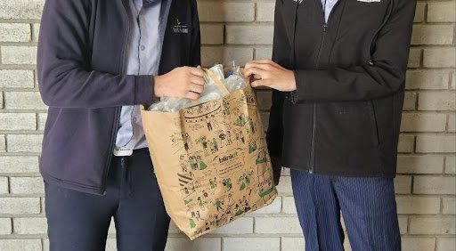 Two students handing over a bag of collected plastic
